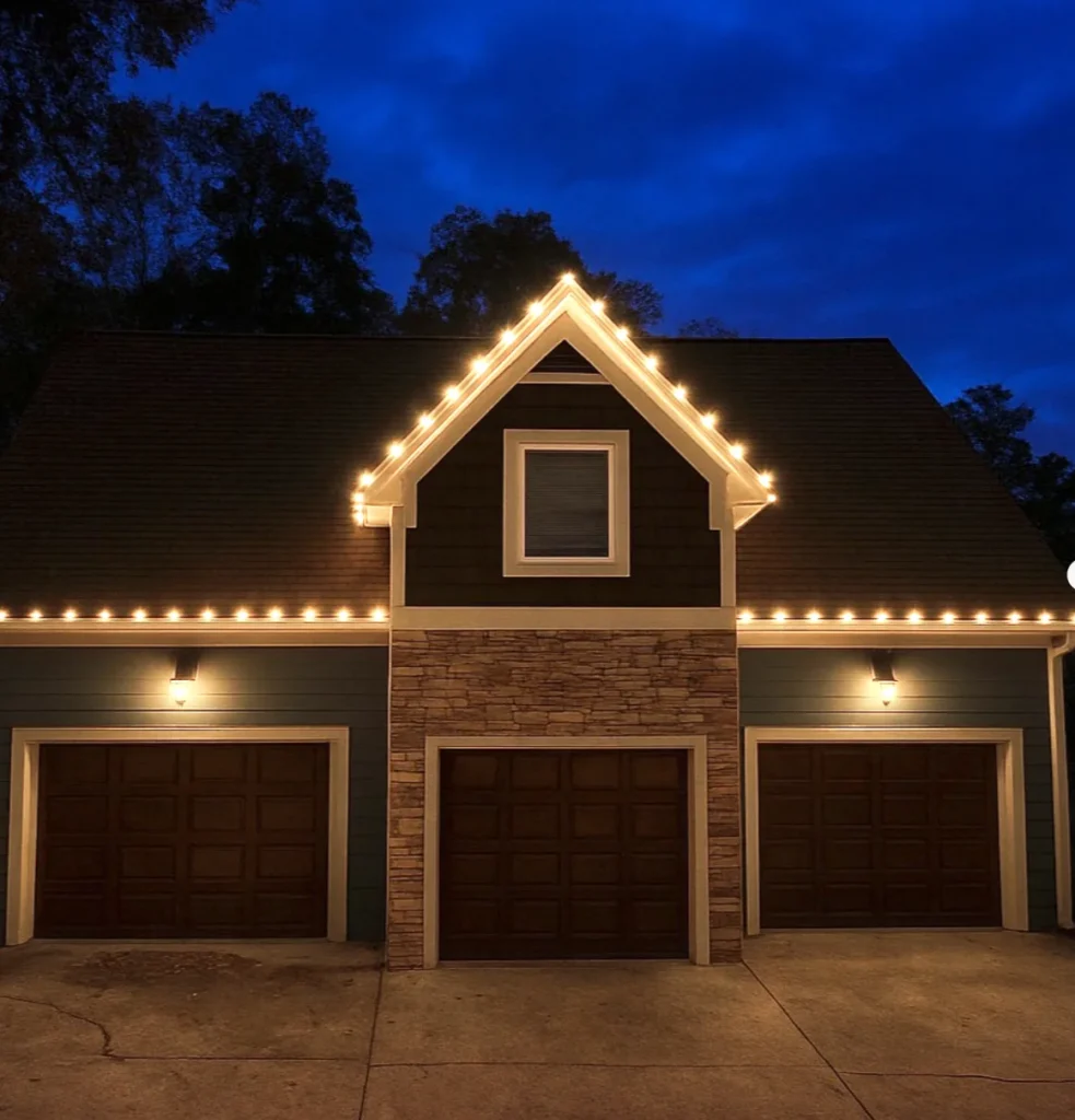 Garage and gable roofline outlined with warm white Christmas lights at dusk