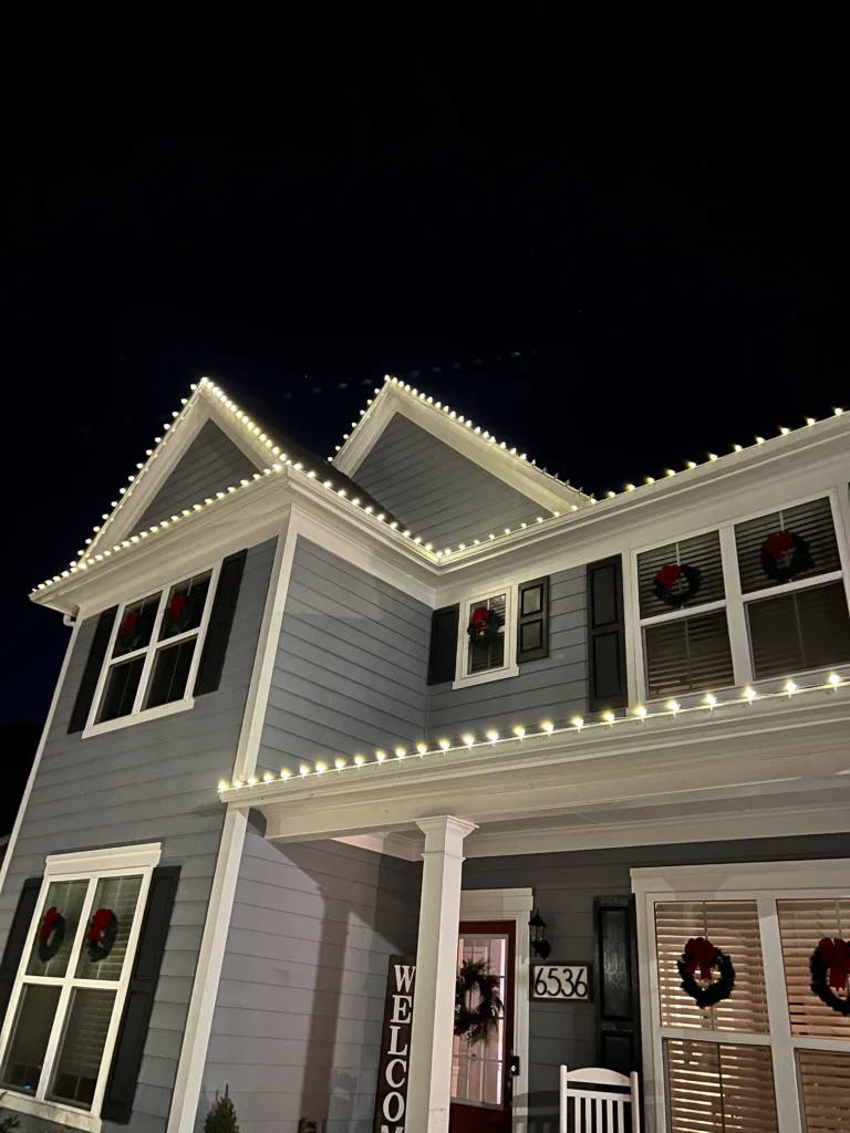 Close view of warm white Christmas lights installed along residential roofline eaves and architectural peaks